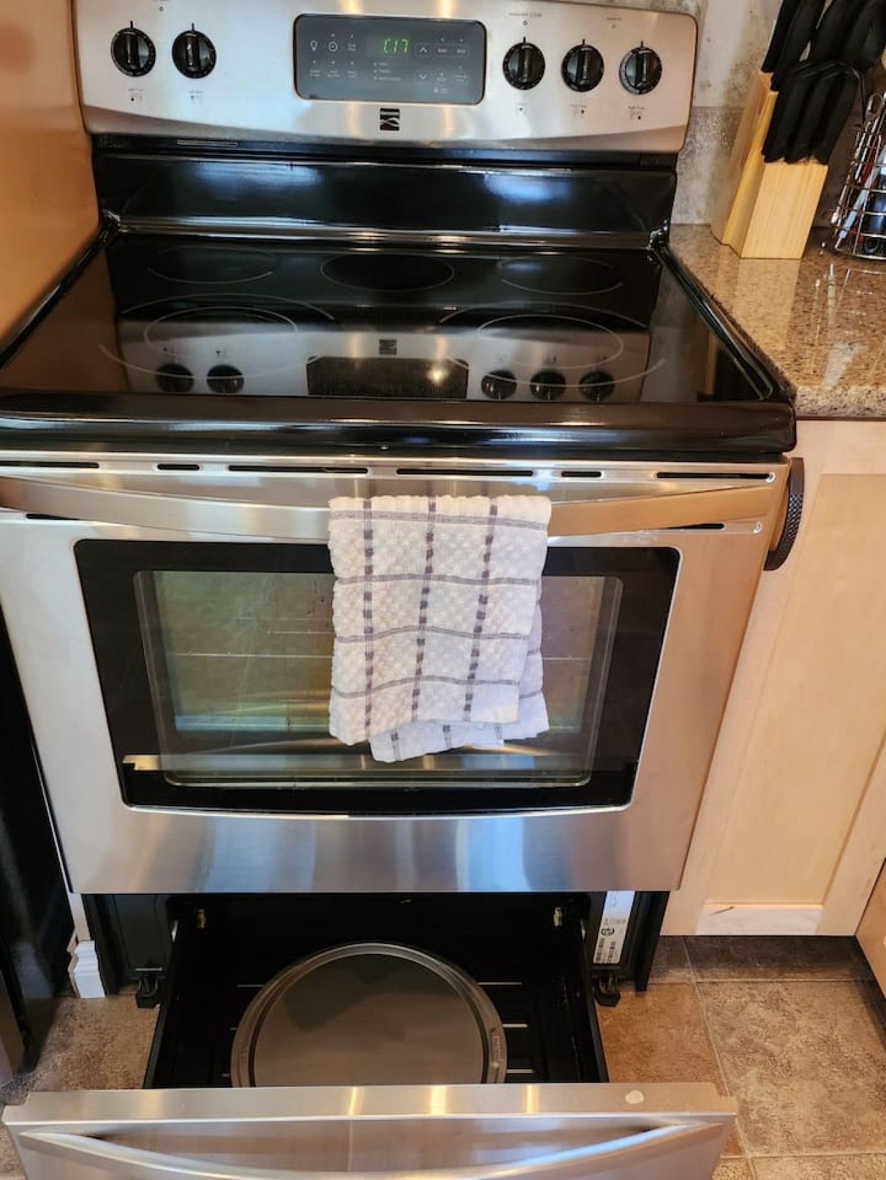 A kitchen with a stainless steel stove and oven, a towel hanging inside the oven, and a knife rack on the countertop.