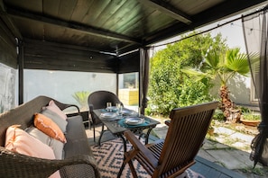 A covered patio with a table set for dining, wicker furniture, and potted plants.
