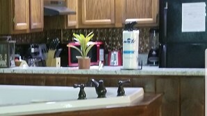 Una cocina con armarios de madera, un refrigerador negro y una encimera con un lavamanos y tres grifos negros.