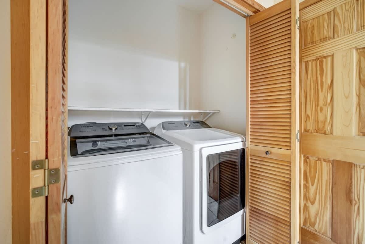 Een praktische wasruimte met een voorlader wasmachine en droger, een houten deur en een klein raam.