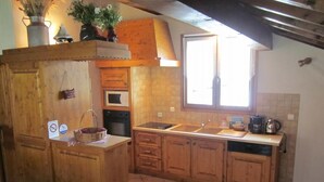 A kitchen with wooden cabinets, a central island, a window, and a tiled floor. - GITE LA GRANDE ROCHE (CHAMPAGNY EN VANOISE)