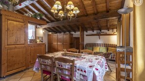 A rustic wooden interior with a dining table set for four, wooden cabinets, and a cozy seating area with a checkered sofa. - GITE LA GRANDE ROCHE (CHAMPAGNY EN VANOISE)