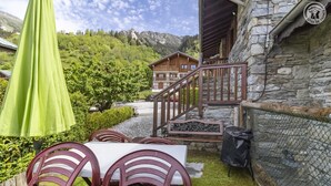 A patio with outdoor seating, a stone building, and a mountain backdrop. - GITE LA GRANDE ROCHE (CHAMPAGNY EN VANOISE)