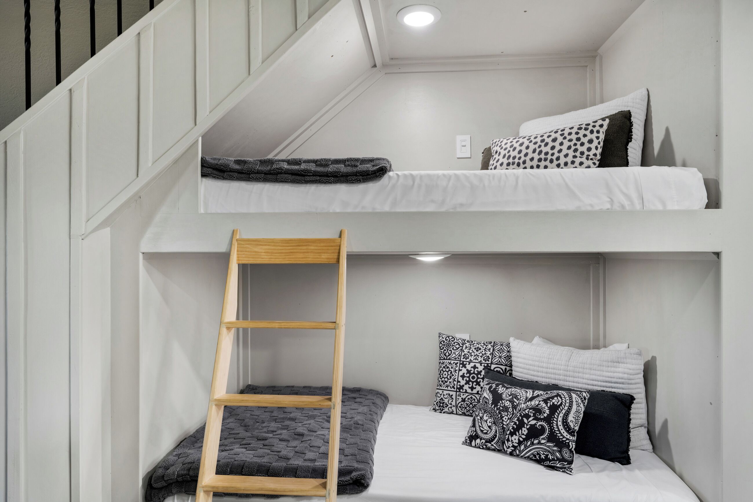 Dormitorio con literas, una escalera de madera, ropa de cama blanca y almohadas estampadas.