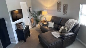 Sala de estar com sofá de couro marrom, TV montada na parede, planta em vaso, abajur e lareira.