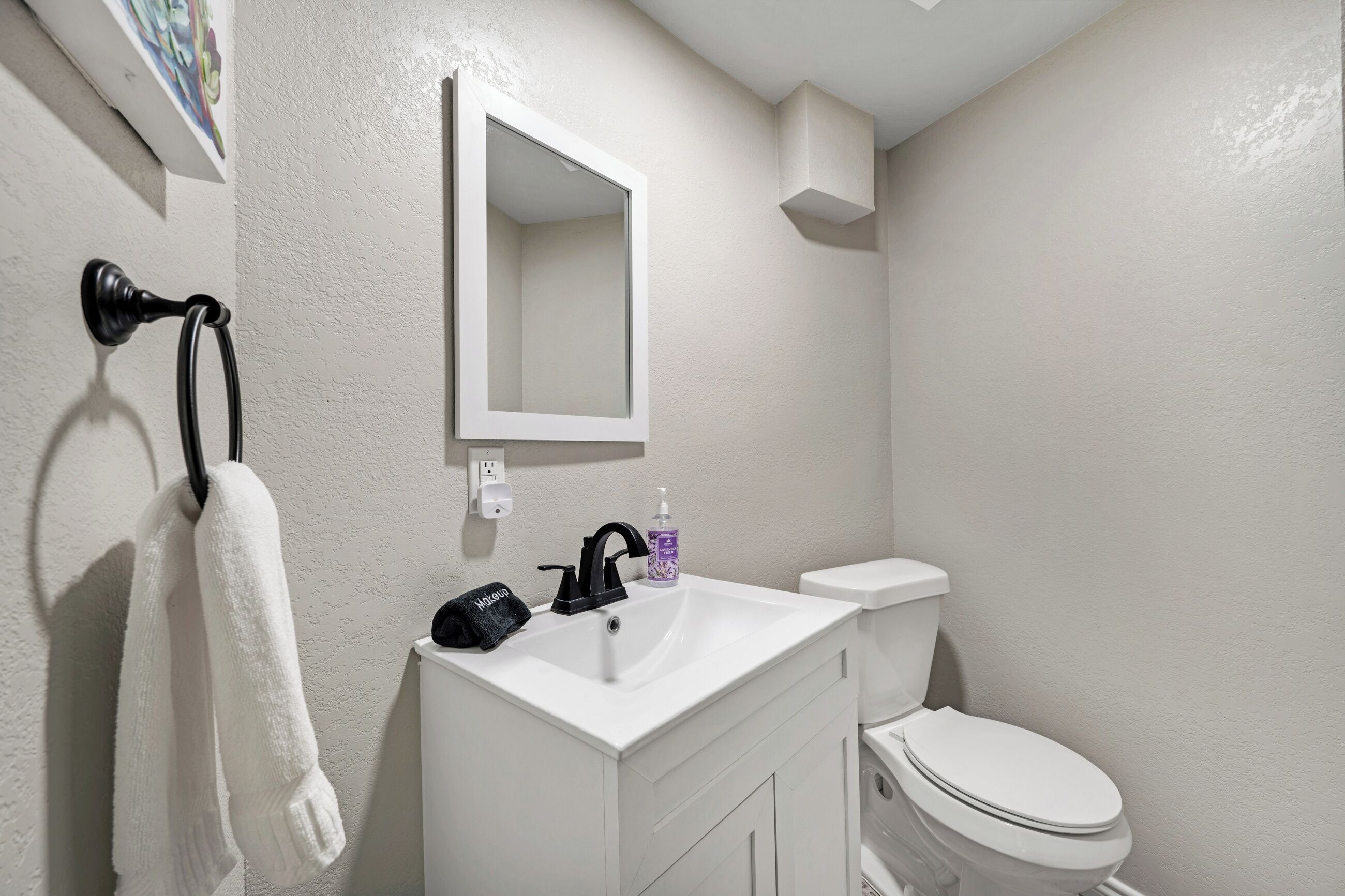 A bathroom with a white sink, a black faucet, a white toilet, and a towel hanging on a hook.