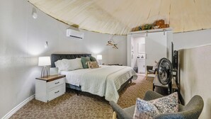 Um quarto com cama, mesas de cabeceira, um ventilador e uma cadeira.