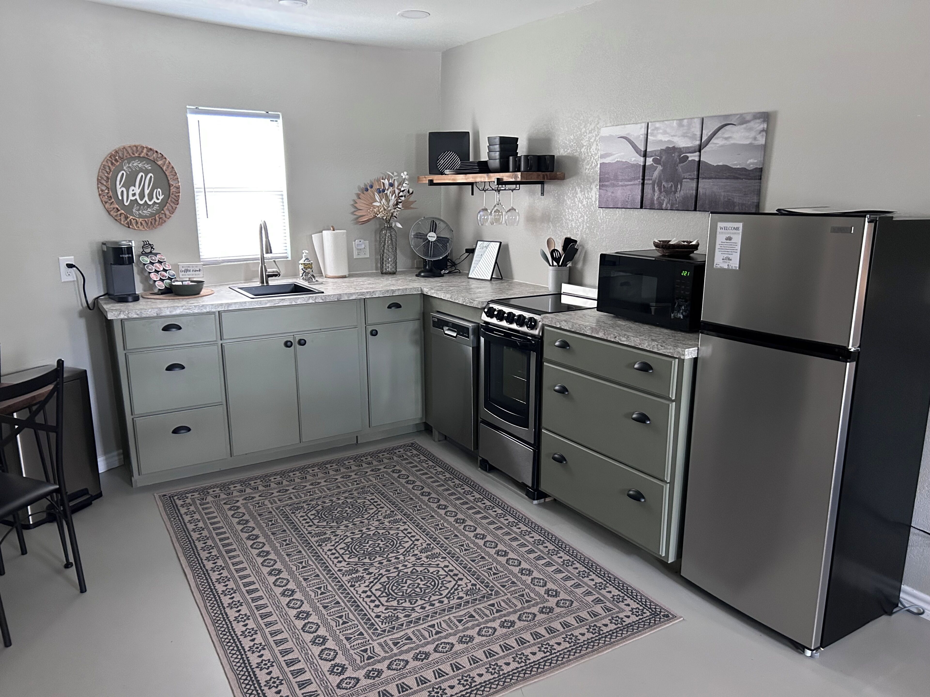A modern kitchen with grey cabinets, a stainless steel refrigerator, a microwave, and a built-in oven.