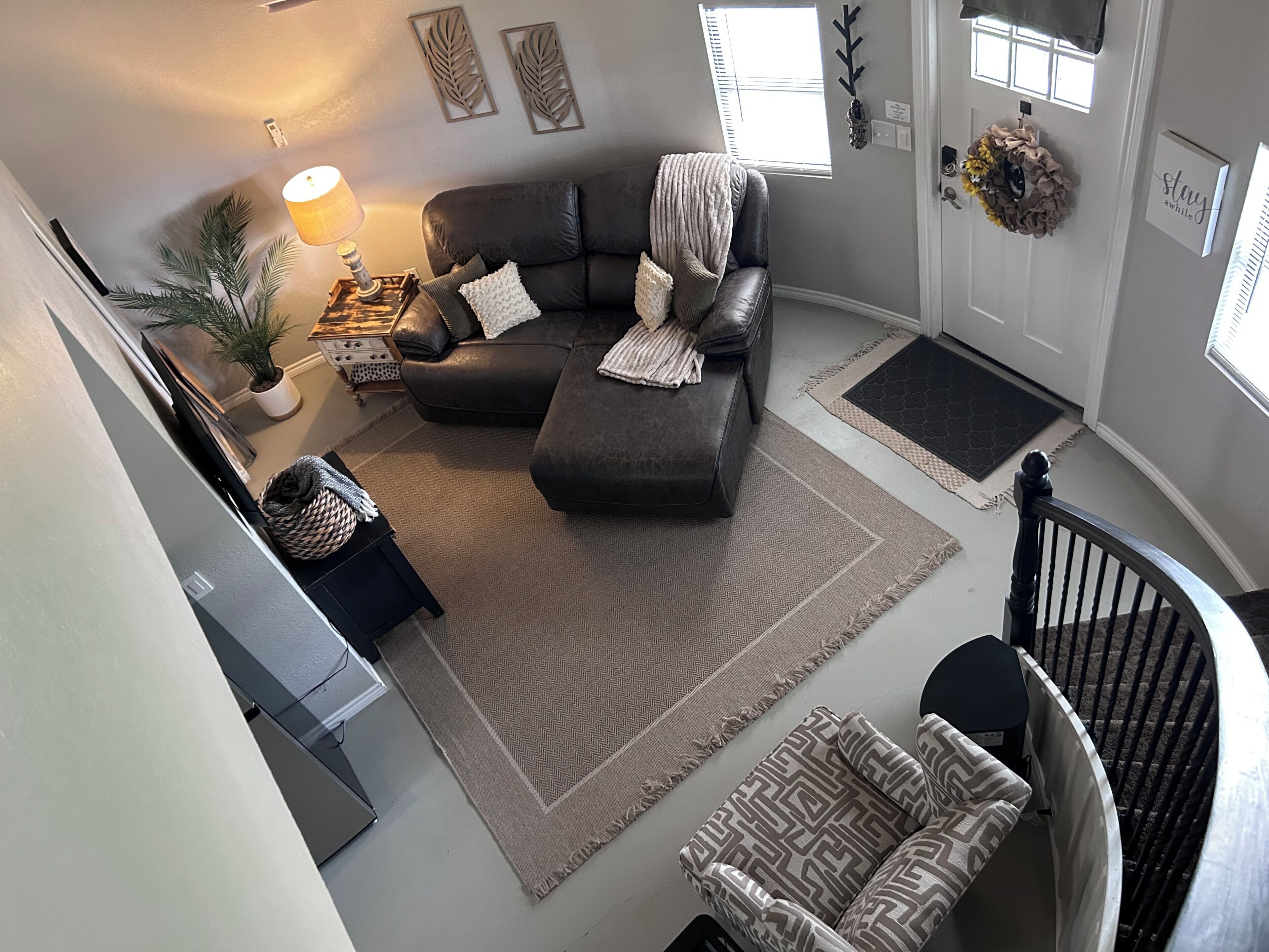 A living room with a sectional sofa, a patterned armchair, a coffee table, a lamp, a potted plant, and a staircase.