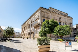 A historic building with classical architecture, a paved courtyard, and potted plants.