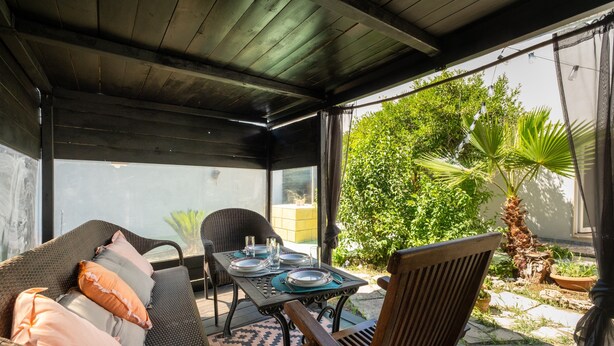 Eine überdachte Terrasse mit Esstisch, Korbmöbeln und Blumentöpfen.