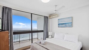 A hotel room with a large bed, a ceiling fan, a painting of the ocean, and a view of the sea through a balcony. - Front Row to the Tide at Imperial Surf (Gold Coast)