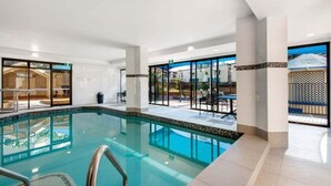 A swimming pool with clear water, surrounded by a tiled deck and glass doors leading to an outdoor area. - Front Row to the Tide at Imperial Surf (Gold Coast)