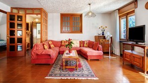 A living room with a sectional sofa, a coffee table, a television, and a large window. - Apartment 'Casa Lella Clemy' with Mountain View, Balcony and Wi-Fi (Aymavilles)