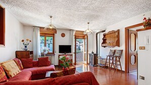A living room with a red sofa, a television, a wooden cabinet, and a painting on easels. - Apartment 'Casa Lella Clemy' with Mountain View, Balcony and Wi-Fi (Aymavilles)
