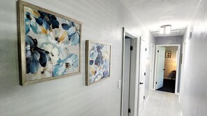A hallway with two floral paintings on the wall, white tiled flooring, and doors leading to other rooms. - Blue Door House ! (Lakeland)