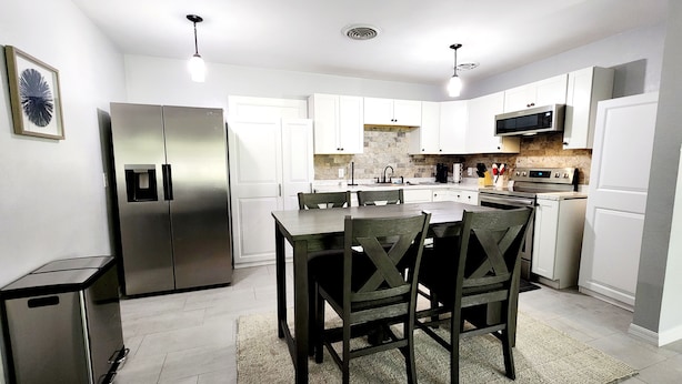 A modern kitchen with white cabinets, a stainless steel refrigerator, a microwave, and a built-in oven. - Blue Door House ! (Lakeland)