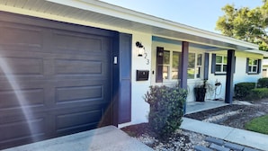 A two-story house with a dark garage door, a small porch with a potted plant, and a mailbox with the number 23. - Blue Door House ! (Lakeland)