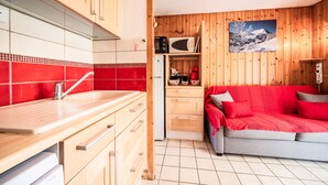 A compact kitchen with wooden cabinets, a red tiled backsplash, a microwave, and a refrigerator. - Apartment 'Appartement Les Oursons' with Mountain View, Balcony and Wi-Fi (Morillon)