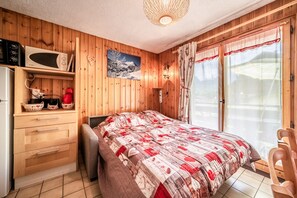 Quarto com painéis de madeira, uma cama, micro-ondas, frigorífico e um armário de madeira.