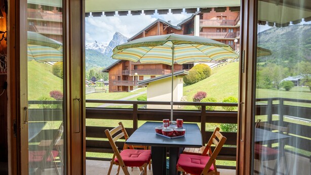 A balcony with a table, chairs, and a striped umbrella. - Apartment 'Appartement Les Oursons' with Mountain View, Balcony and Wi-Fi (Morillon)