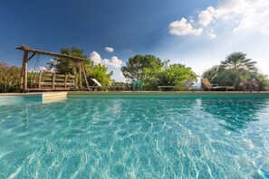 A clear swimming pool with a wooden swing set and a small structure in the background.