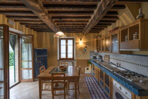 A rustic kitchen with wooden beams, a dining table, chairs, a window, and a sink.