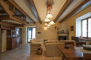 A spacious living area with a high ceiling, wooden beams, a fireplace, and a dining table.