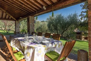 An outdoor dining area with a table set for four, surrounded by wooden chairs with green cushions.