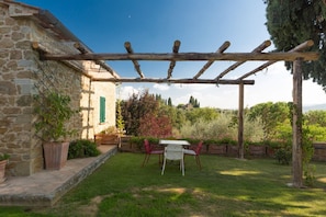A stone building with a pergola, a table with chairs, and a garden with potted plants.