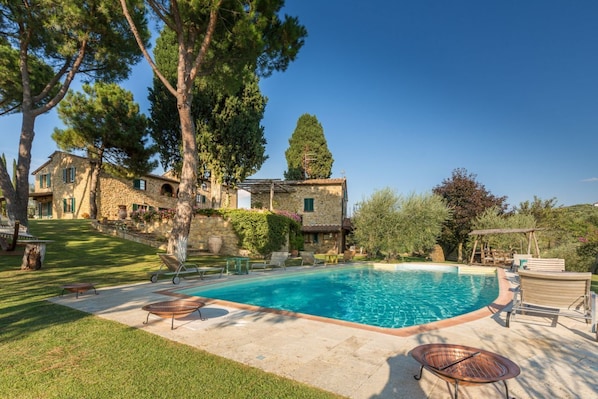 A stone house with a swimming pool, outdoor seating, and a well-maintained lawn.