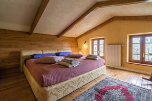 A bedroom with a wooden ceiling, a bed with multiple pillows, a radiator, and a window with a view.
