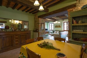 A rustic dining area with a table set for four, wooden chairs, a stone fireplace, and a stone wall.