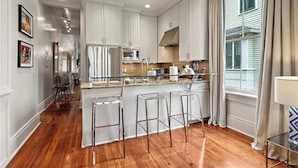 Una cocina moderna con armarios blancos, una isla central con taburetes y un microondas, además de un fregadero.