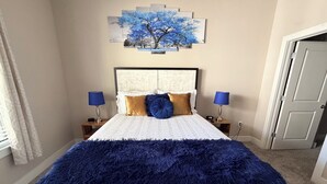 A bedroom with a bed, two bedside tables, a nightstand, a blue lamp, a painting of trees, and a door. - POOL VIEW/DOWNTOWN DALLAS/MEDICAL DISTRICT/DALLAS LOVE FIELD (Dallas)