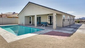 Een modern huis met een zwembad, overdekt terras en een omheinde achtertuin.