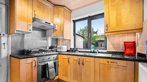 A modern kitchen with wooden cabinets, stainless steel appliances, and a large window offering a view of the outdoors. - Stunning 2-bed House in Birmingham (Birmingham)