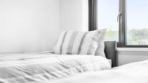 A neatly made bed with striped pillows and a gray headboard, positioned next to a window with a view of greenery. - Stunning 2-bed House in Birmingham (Birmingham)