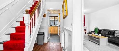 A staircase with red carpet, a kitchen area, and a living room with a black sofa.