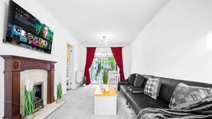 A modern living room with a fireplace, a flat-screen TV mounted on the wall, a black leather sofa, and a coffee table. - Stunning 2-bed House in Birmingham (Birmingham)