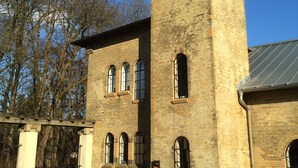 A brick building with a tower, arched windows, and a metal roof. - Vacation apartment in the tower  (Lehmkuhlen)