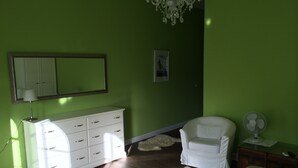 A room with green walls, a white dresser, a white chair, a bed, a chandelier, and a fan. - Vacation apartment in the tower  (Lehmkuhlen)