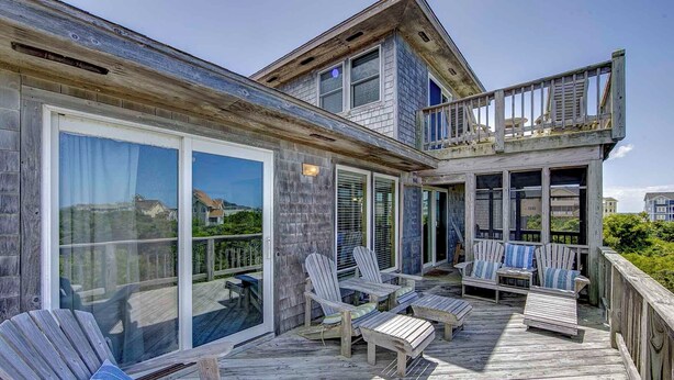 A wooden deck with Adirondack chairs and a glass door leading to a covered area. - Oceanside, Ocean Views, Sound Views, Sundeck, Short Walk To The Beach! (Hatteras)