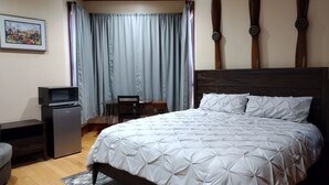 A neatly arranged bedroom with a bed, a desk, a chair, a television, and a small refrigerator.