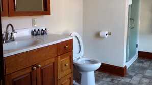A bathroom with a white toilet, wooden vanity with a mirror, and a sink with toiletries.