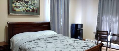 Una camera da letto con un letto, una scrivania, una sedia, una televisione e un quadro appeso al muro.