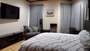 A bedroom with a bed, a TV, a desk, a chair, and curtains.