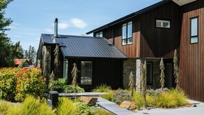 Uma casa moderna com telhado de metal, fachada de madeira e um jardim ajardinado com diversas plantas e um caminho.