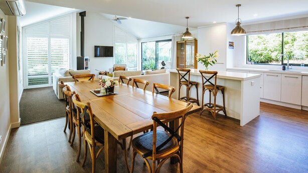 Uma cozinha moderna com mesa de jantar de madeira, armários brancos e uma janela grande com vista para vegetação.