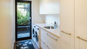 Uma cozinha compacta com máquina de lavar, pia e vista para um jardim através de uma porta.